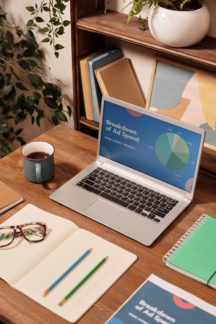 experience-img Laptop displaying ad spend data on a wooden desk with office supplies.